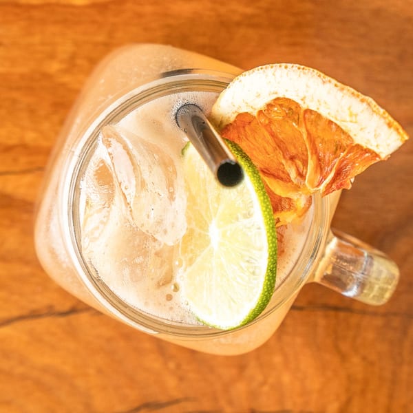 Overhead view of a drink with ice, lime, and dried orange in a glass jar on wood.