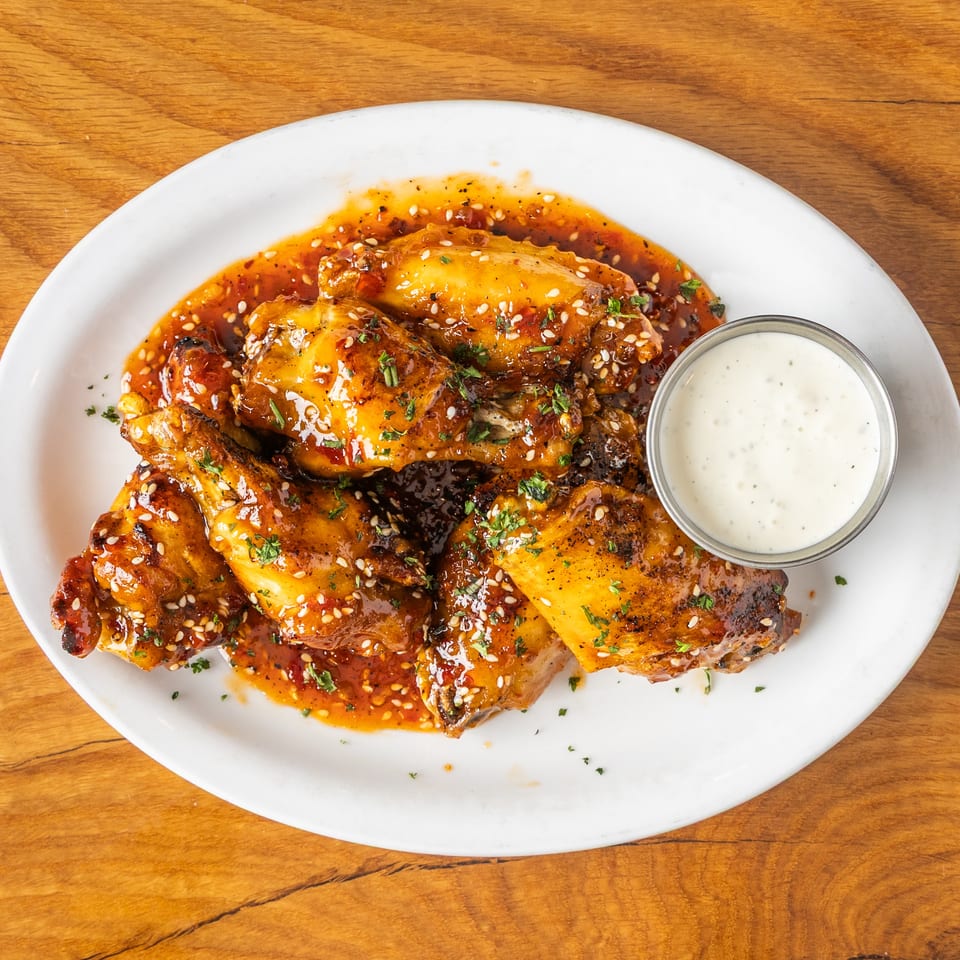Sweet chili glazed chicken wings with sesame seeds, parsley, and a side of creamy dip.