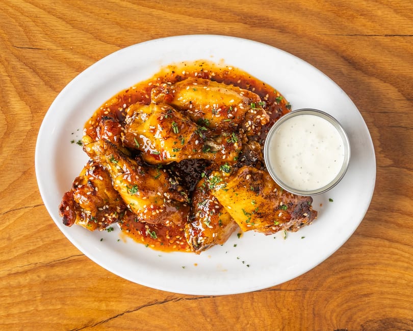 Sweet chili glazed chicken wings with sesame seeds, parsley, and a side of creamy dip.