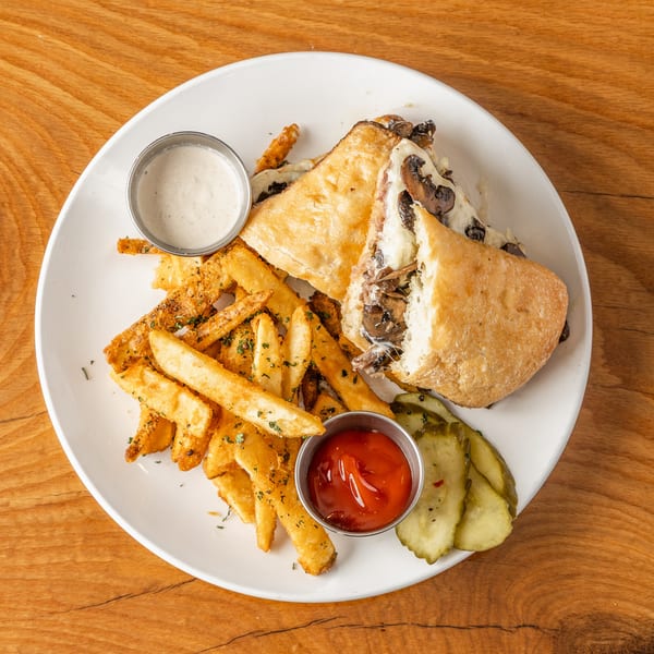 Mushroom and cheese panini with golden fries, ketchup, ranch, and pickles on a white plate.