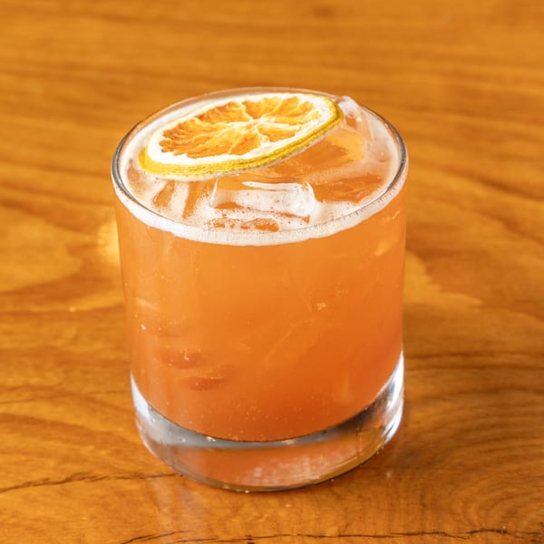 Orange cocktail with ice and a dried orange slice on a wooden table.