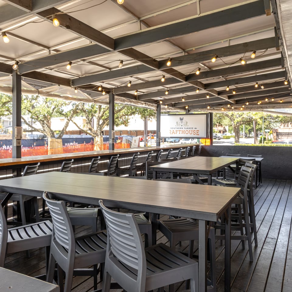 Empty outdoor patio at Southern Yankee Rafterhouse with tall tables, chairs, and string lights.
