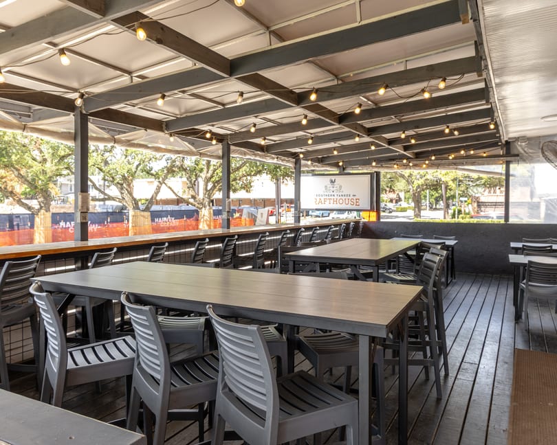 Empty outdoor patio at Southern Yankee Rafterhouse with tall tables, chairs, and string lights.