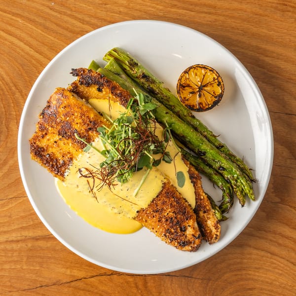 Crispy fish fillets with creamy sauce, grilled asparagus, microgreens, and charred lemon.