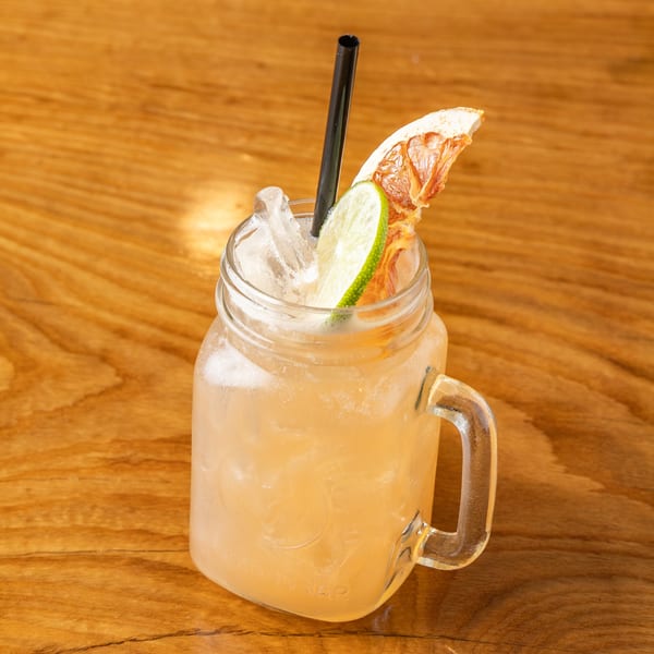 Mason jar cocktail with ice, black straw, lime slice, and dried citrus on a wooden table.