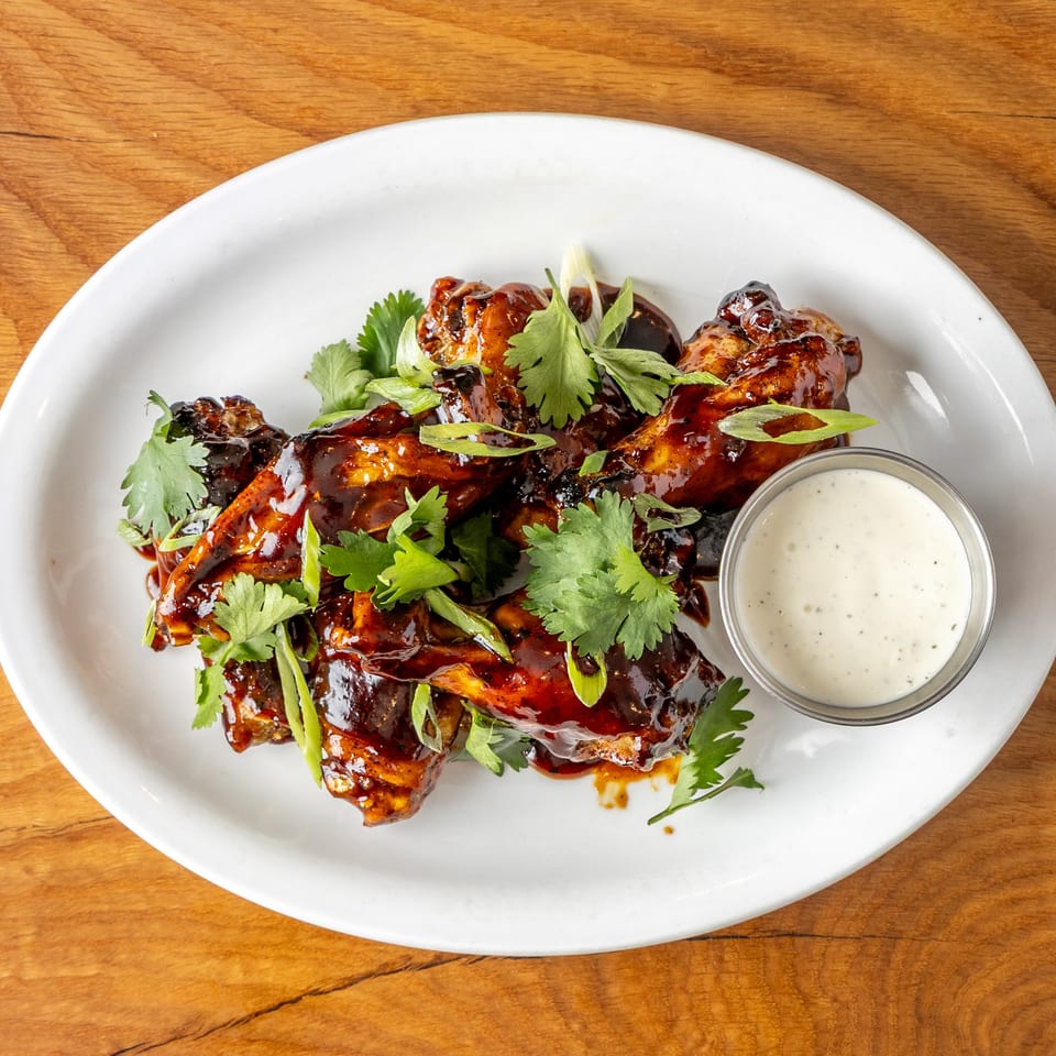 Dark glazed chicken wings topped with cilantro and green onions, served with a creamy dip.