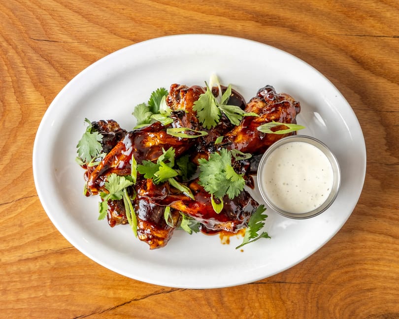 Dark glazed chicken wings topped with cilantro and green onions, served with a creamy dip.