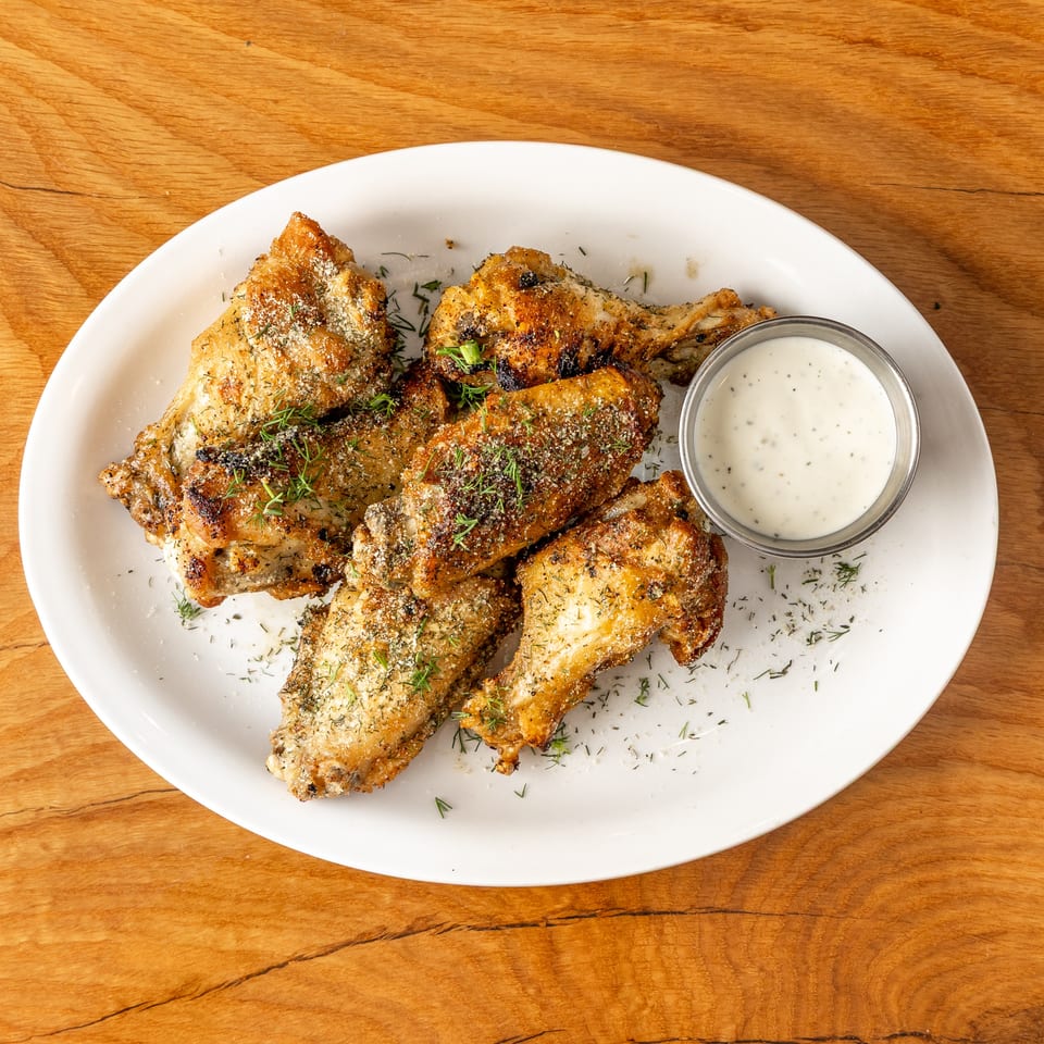 Crispy chicken wings seasoned with dill and parmesan, served on a white plate with ranch.