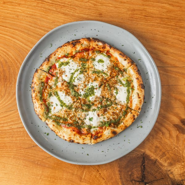 Round pizza with mozzarella, pesto drizzle, and crumbled sausage on a grey plate.