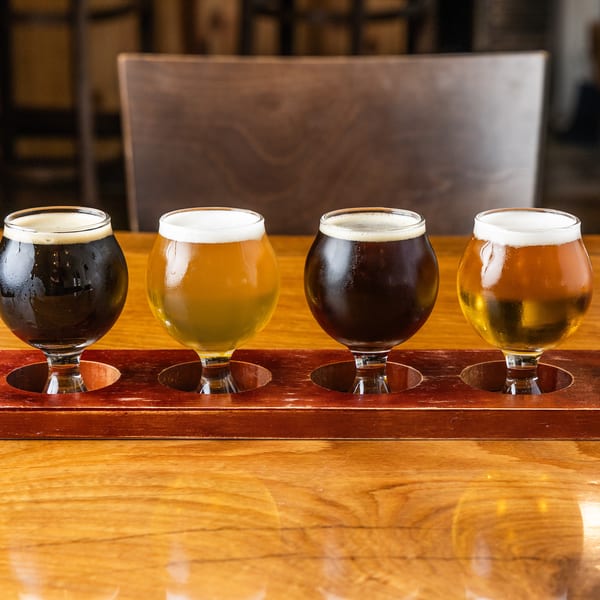 A flight of four beers, two dark and two light, on a wooden table.