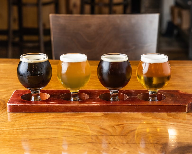 A flight of four beers, two dark and two light, on a wooden table.