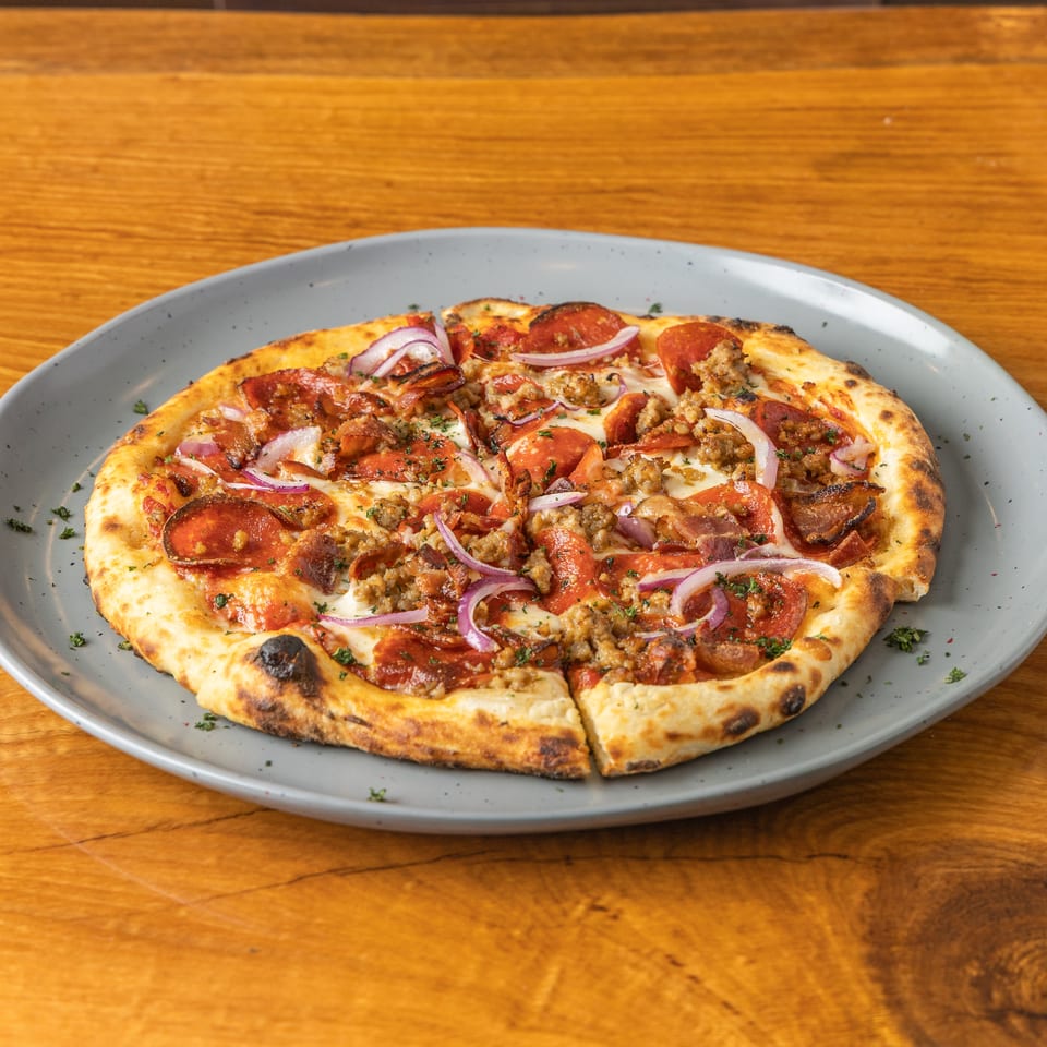 Wood-fired pizza topped with pepperoni, sausage, and red onions on a grey plate.