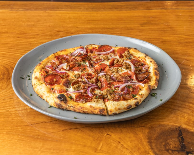 Wood-fired pizza topped with pepperoni, sausage, and red onions on a grey plate.