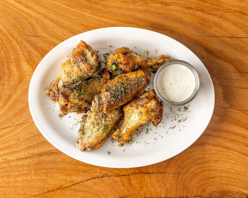 Golden brown chicken wings seasoned with herbs and cheese, served with ranch dip on a white plate.