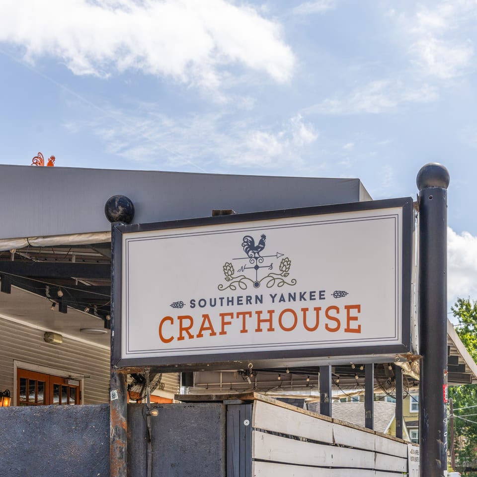 White Southern Yankee Crafthouse sign with a rooster logo, under a bright blue sky.