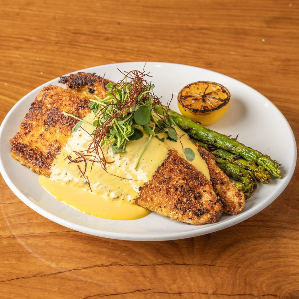 Crispy fried fish fillets with yellow sauce, microgreens, grilled asparagus, and a charred lemon.