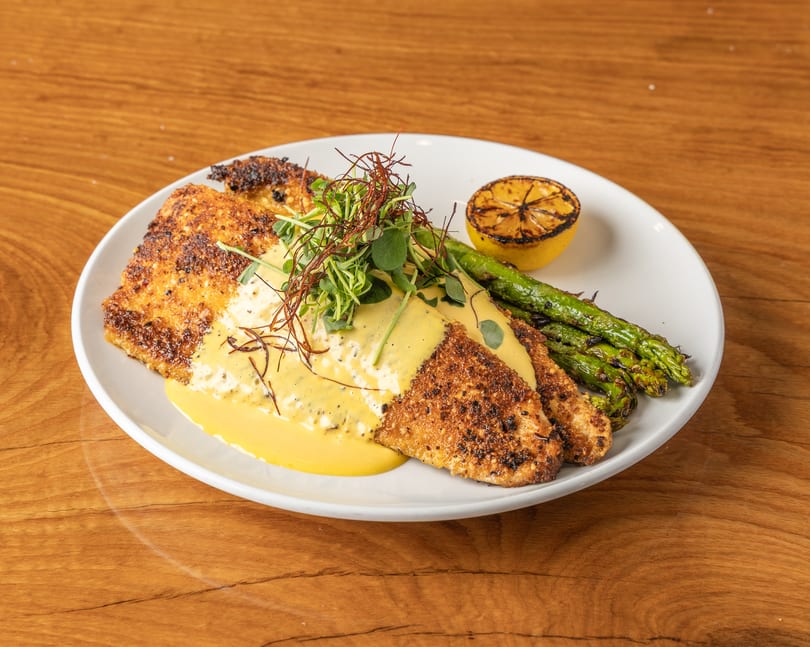 Crispy fried fish fillets with yellow sauce, microgreens, grilled asparagus, and a charred lemon.