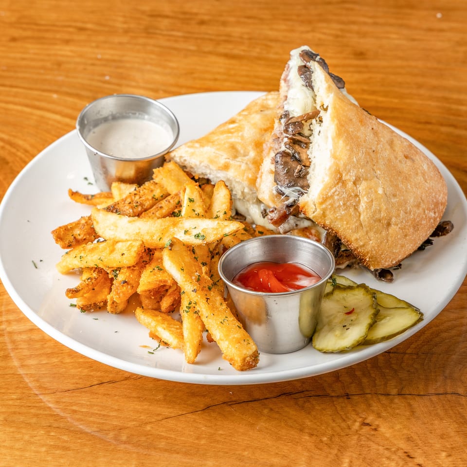 Mushroom and cheese sandwich, seasoned fries, ketchup, ranch, and pickles on a white plate.