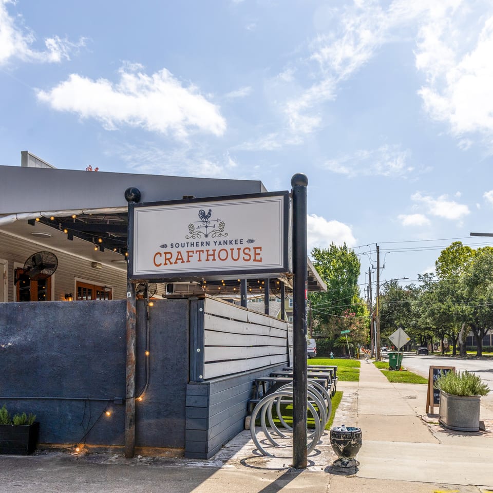 Sunny exterior of Southern Yankee Crafthouse with its sign, outdoor seating, and a tree-lined street.