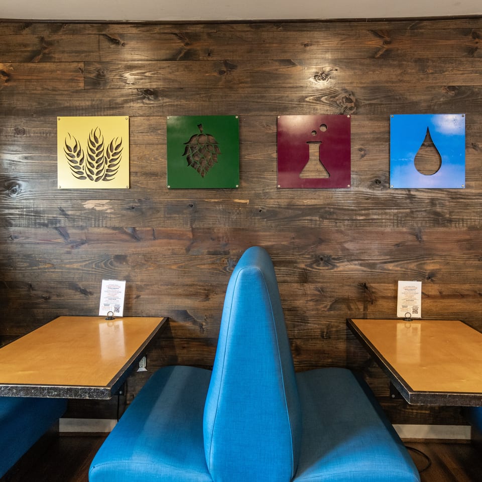 Blue booths and wooden tables in a restaurant with brewing ingredient art on a wooden wall.